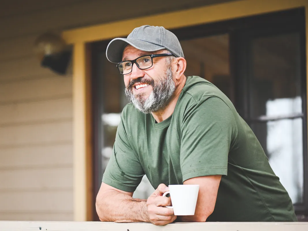 mature man smiling while drinking coffee on his porch