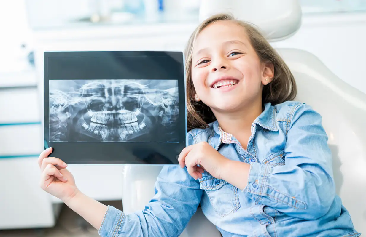 little girl smiling and holding an x-ray of her teeth